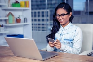 Smiling Asian woman with eyeglasses using smartphone in office