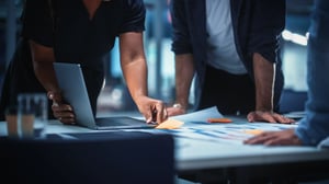 Team members collaborating around a table with a laptop, documents, and notes during a planning meeting